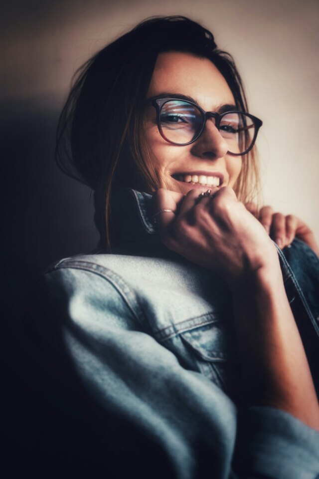 A woman laughing, in glasses and a denim jacket